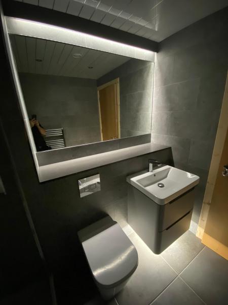 Dark tiled bathroom with an illuminated mirror and wall-mounted sink